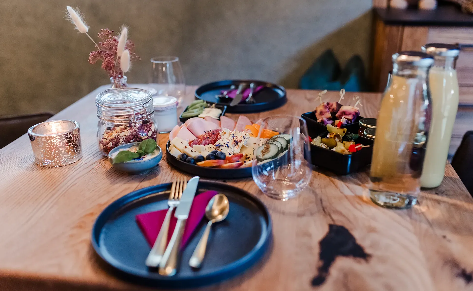 Geschmackvoll gedeckter Tisch mit einer bunten Käseplatte, frischen Snacks, dekorativen Blumen und warmem Kerzenlicht.